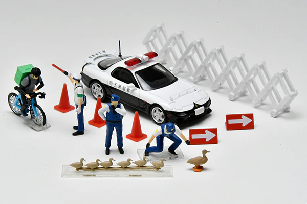 Figure tỉ lệ 1:64 đặt cạnh xe mô hình cảnh sát và phụ kiện rào chắn
